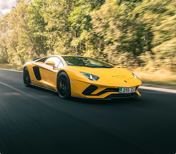 Yellow Lamborghini sports car driving on a road surrounded by trees.