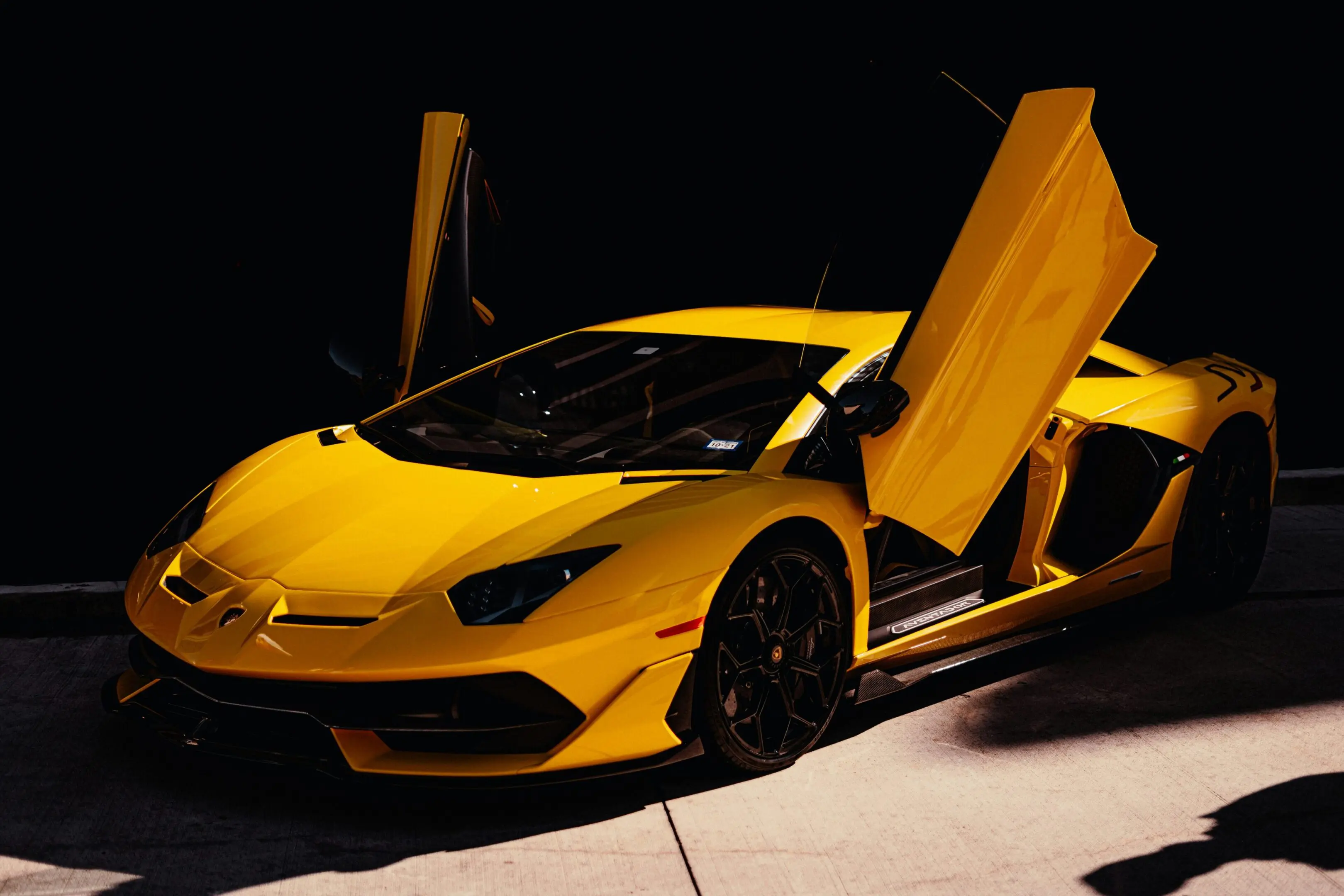 Yellow sports car with scissor doors open at night.