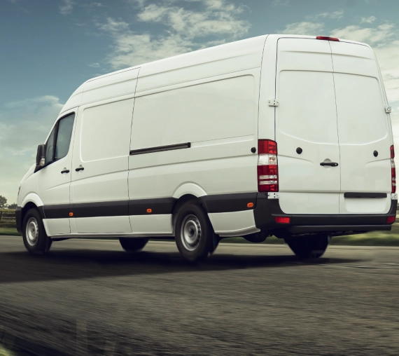 A white cargo van driving on a road under a cloudy sky.