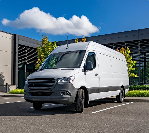 White cargo van parked outside a modern building on a sunny day.